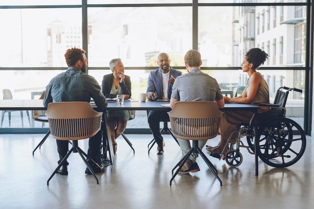 Disability, diversity and business meeting with staff, people or team communication, planning on corporate strategy, goal or mission for KPI. Woman in wheelchair in group talking of company inclusion